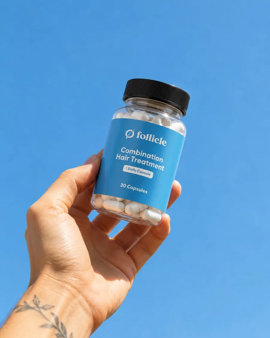 A hand holding a Follicle capsule bottle up against a clear blue sky