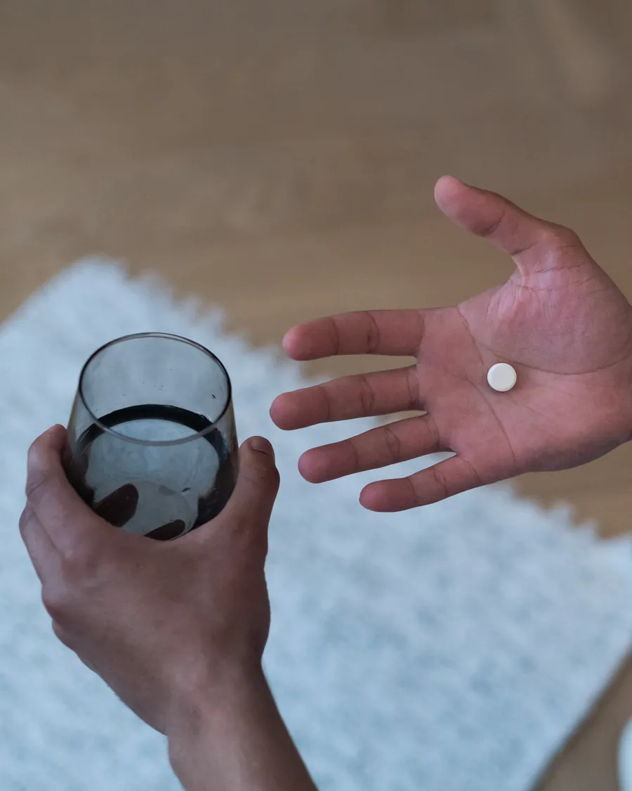 A man holding one white tablet in his palm and a glass of water in his other hand