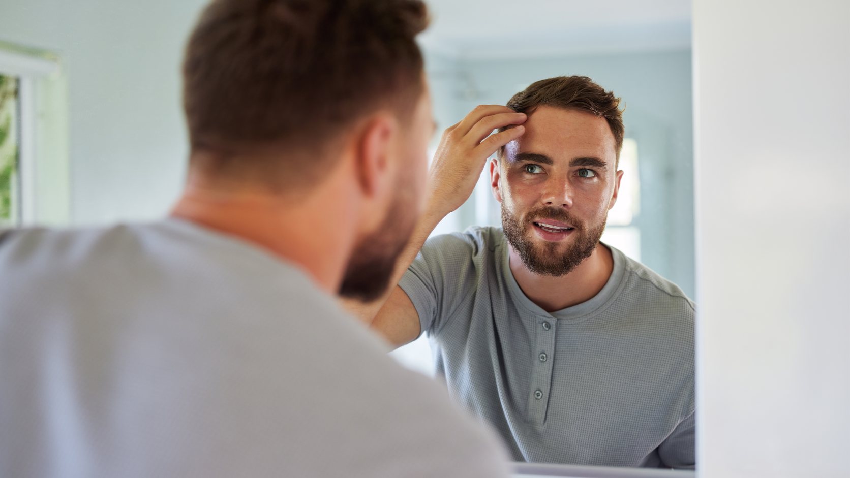 Man checking his hairline in a bathroom mirror